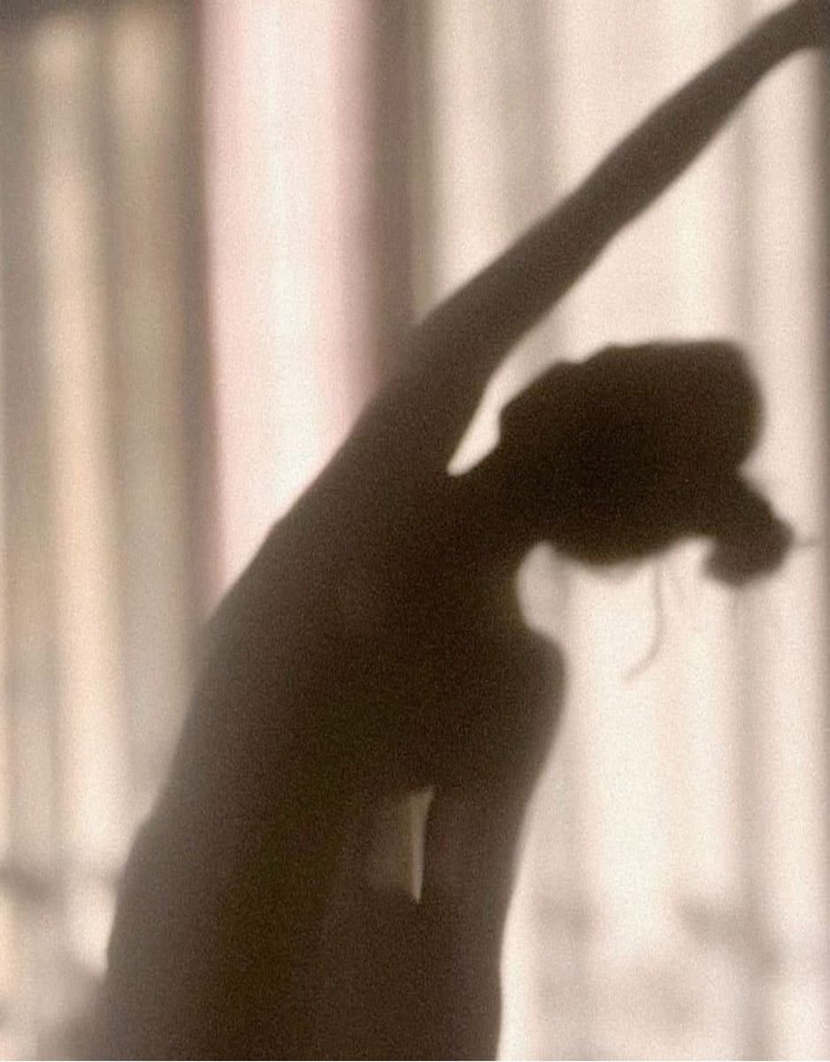 Shadow of a woman stretching one arm overhead against a softly lit wall