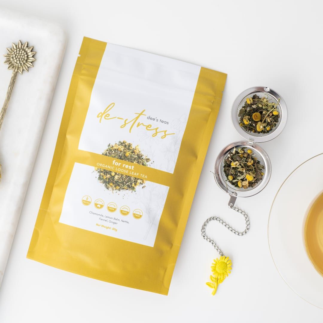 A pack of Dee’s Teas De-Stress Tea beside two tea infusers filled with loose-leaf tea