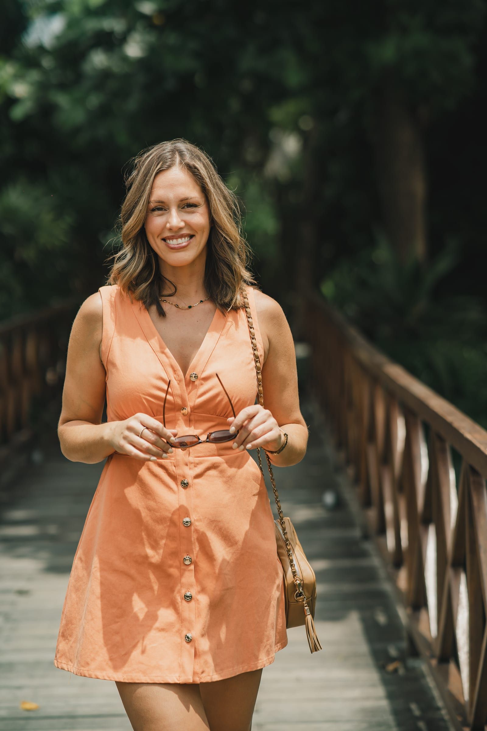 Dee Zibara smiling, wearing an orange dress and holding sunglasses