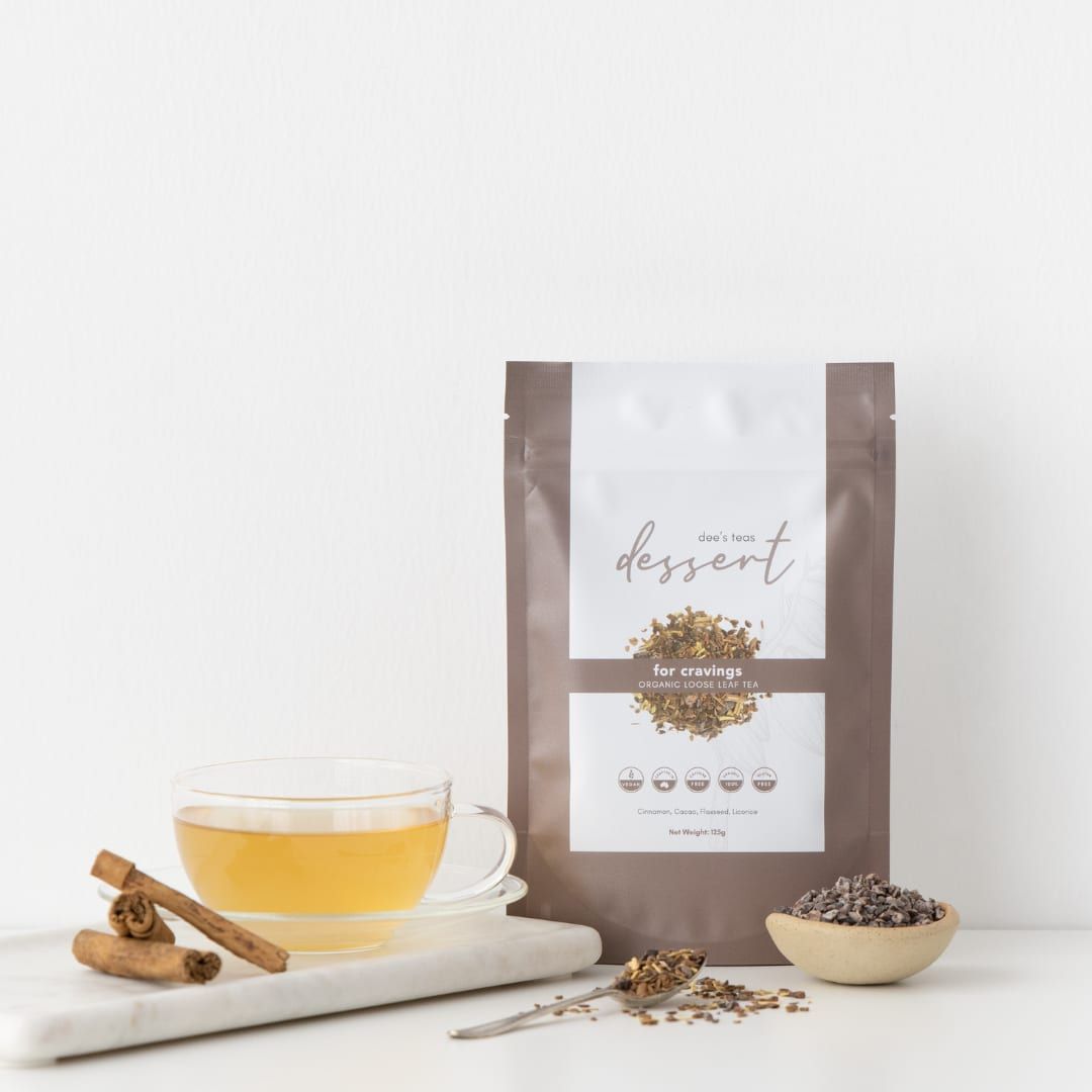 A pack of Dee’s Teas Dessert Tea beside a glass cup of tea and cinnamon sticks