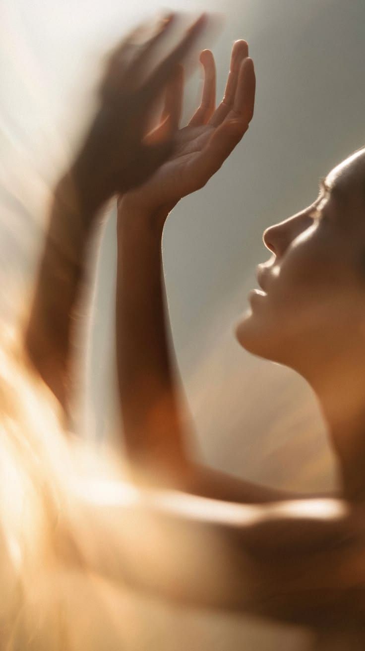 A woman in golden light with her hands raised, eyes closed