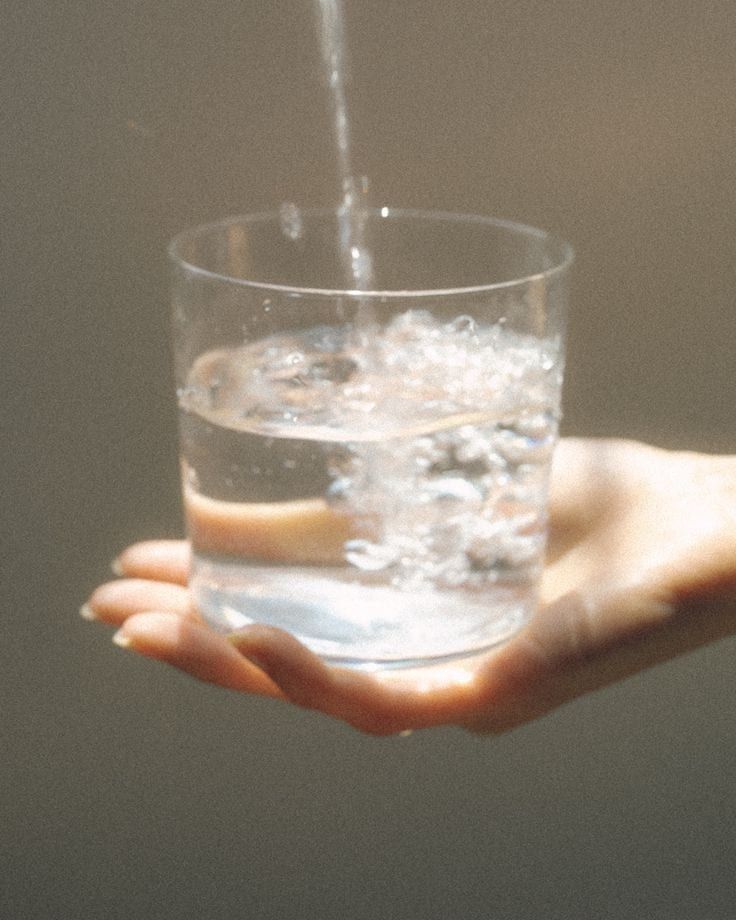 A hand holding a glass as water is poured into it