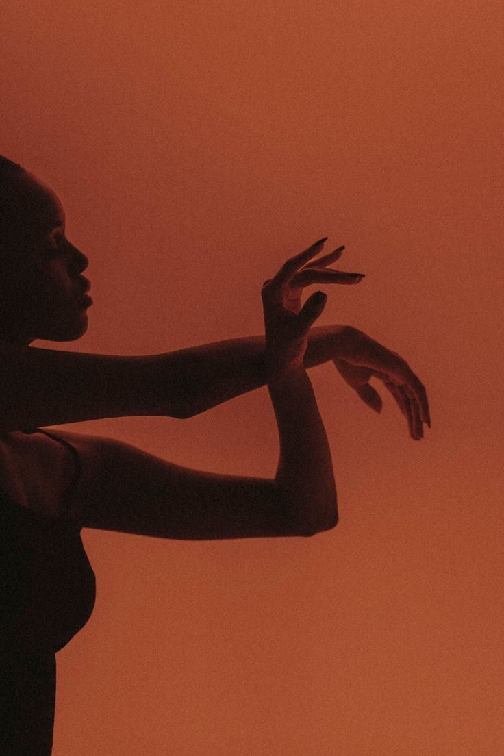 Silhouette of a woman with her hands raised against a rust-coloured wall