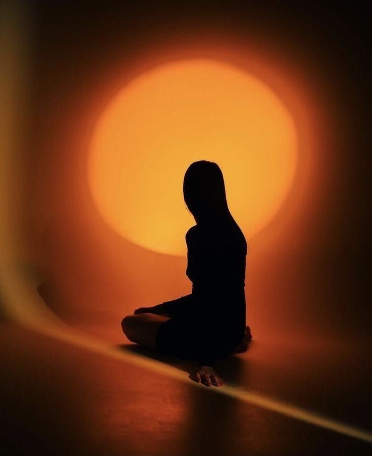 Silhouette of a woman sitting cross-legged in front of a glowing orange light