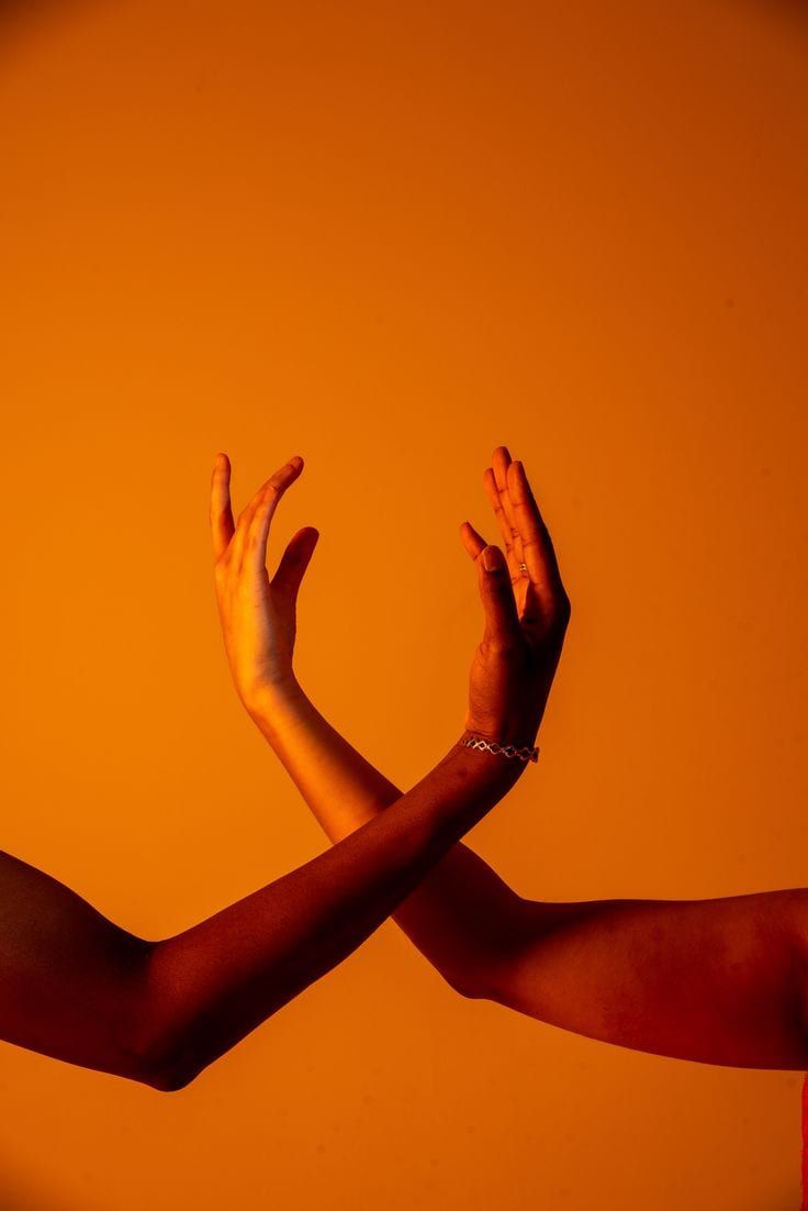 Two arms crossed at the wrists, hands open, against an orange background